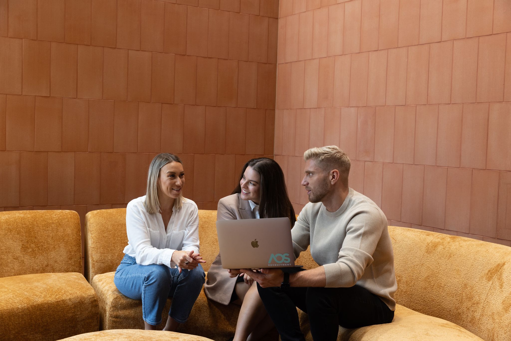 three poeple on a yellow couch working with a laptop