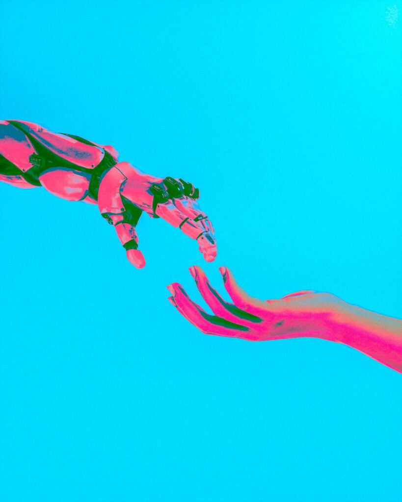 neon pink robot hand and a human hand about to touch against a cyan background