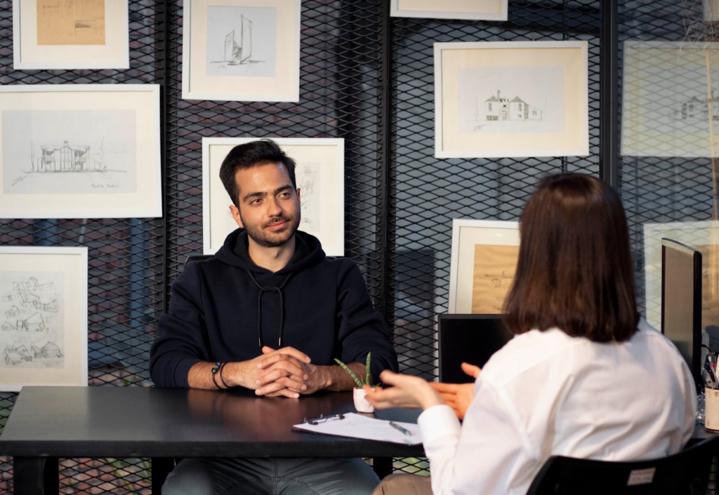man and woman talking across desk with framed art behind