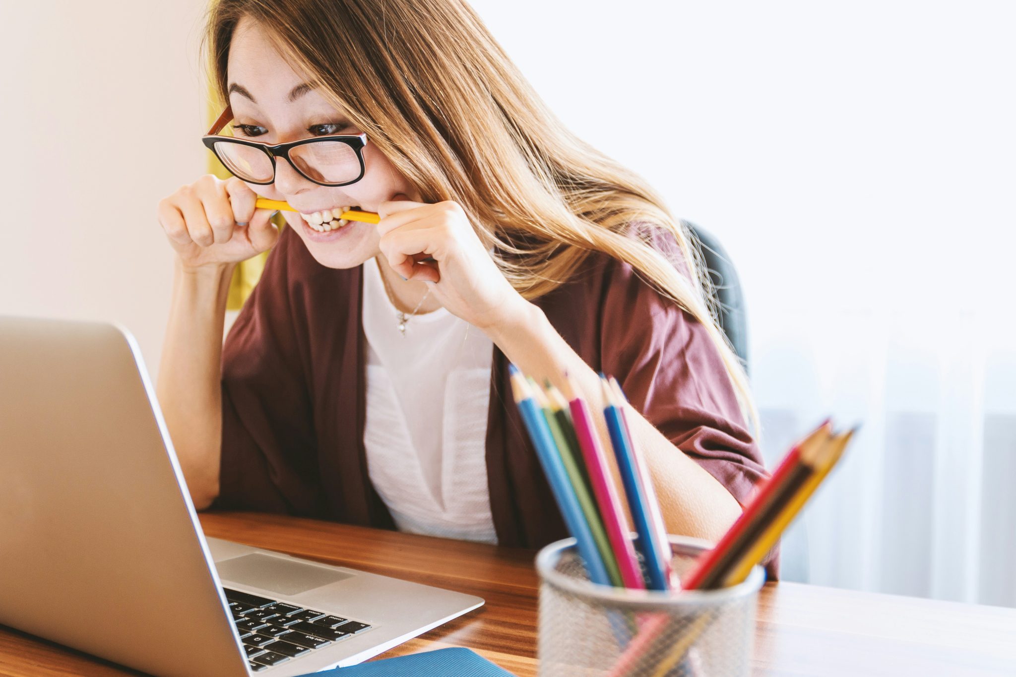 woman biting a pencil looking at her laptop
