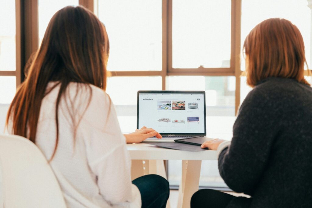 two women working at a laptop from behind