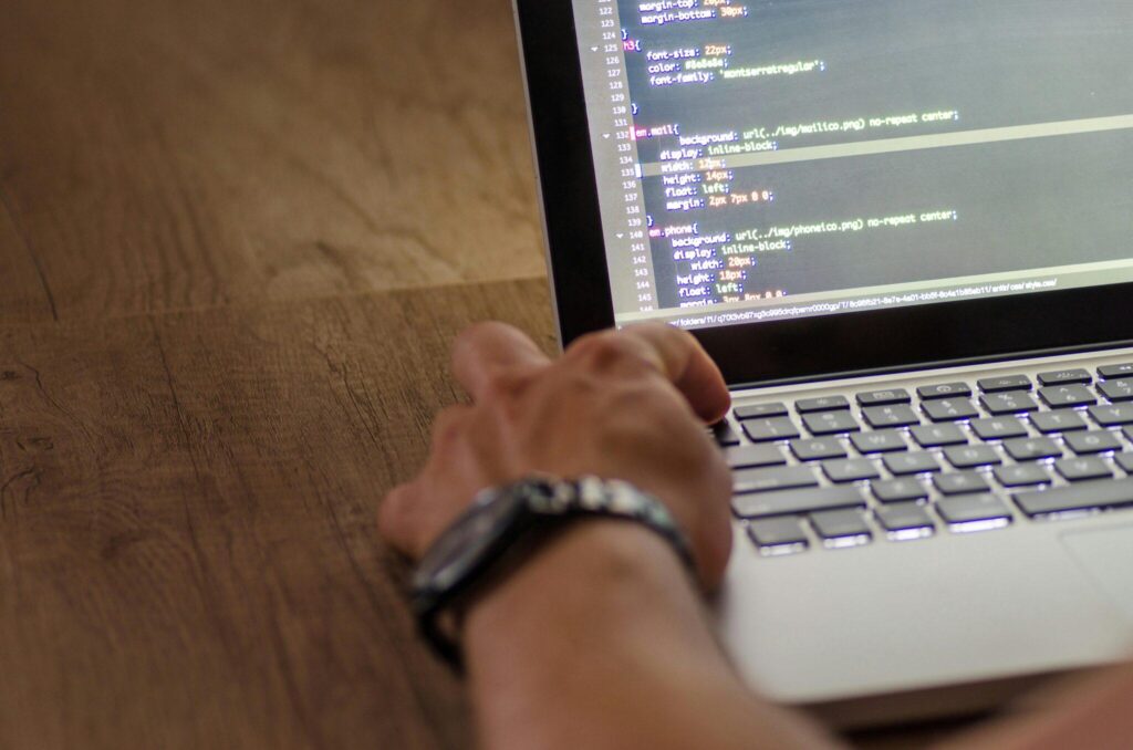 person pressing escape on a laptop with code showing on monitor