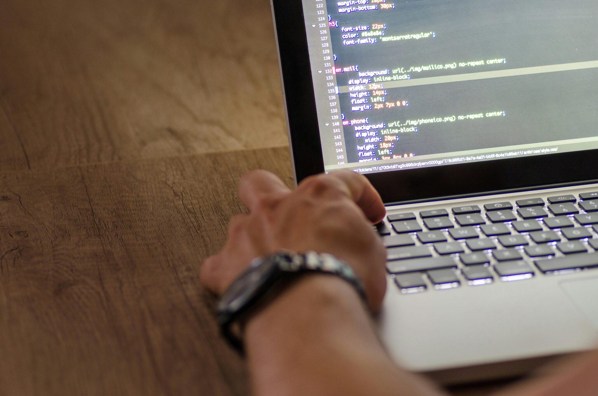 person pressing escape on a laptop with code showing on monitor