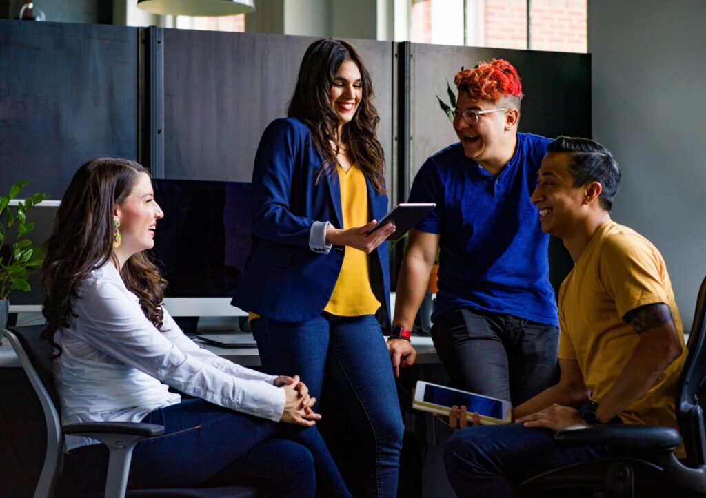 four people in an office holding tablets and ipads and laughing