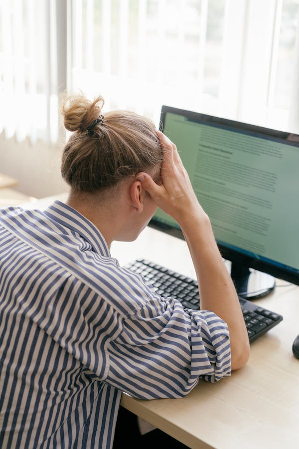 person sitting at desk with their head in their right hand reading text on a monitor